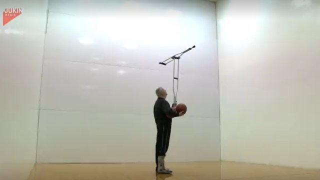 Man balances two crutches on his chin while dribbling basketball