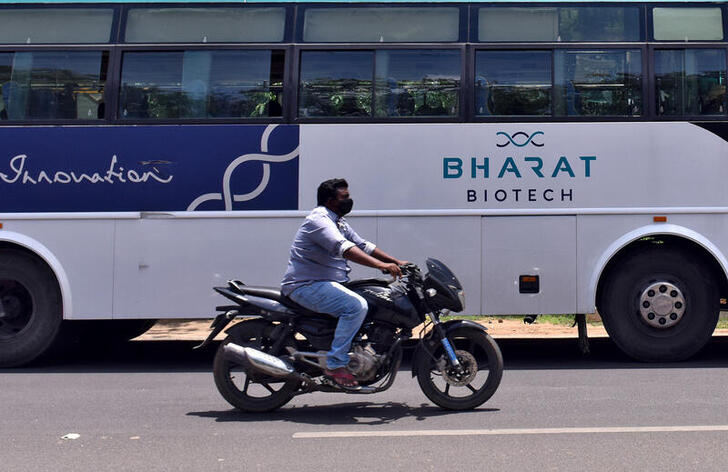 FILE PHOTO: A man rides his motorcycle past a parked bus of Indian biotechnology company Bharat Biotech outside its office in Hyderabad, India July 3, 2020. REUTERS/Stringer/File Photo