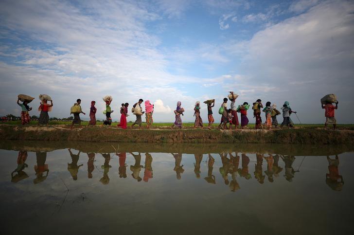Rohingya refugees are reflected in rain water along an embankment next to paddy fields after fleeing from Myanmar into Palang Khali, near Cox's Bazar, Bangladesh November 2, 2017. REUTERS/Hannah McKay 