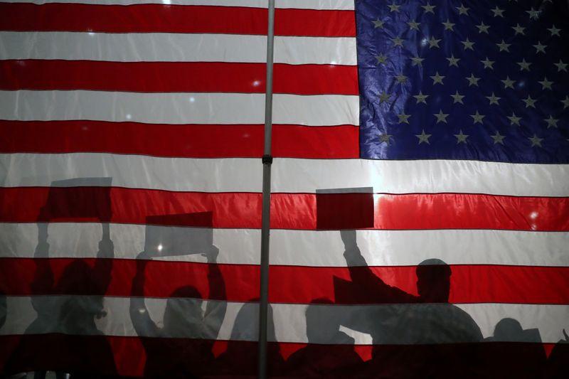Silhouettes of attendees holding signs in front of an American flag are seen during a campaign rally held by Democratic 2020 U.S. presidential candidate and U.S. Senator Bernie Sanders (I-VT), in Sioux City, Iowa, U.S., January 26, 2020. REUTERS/Ivan Alvarado