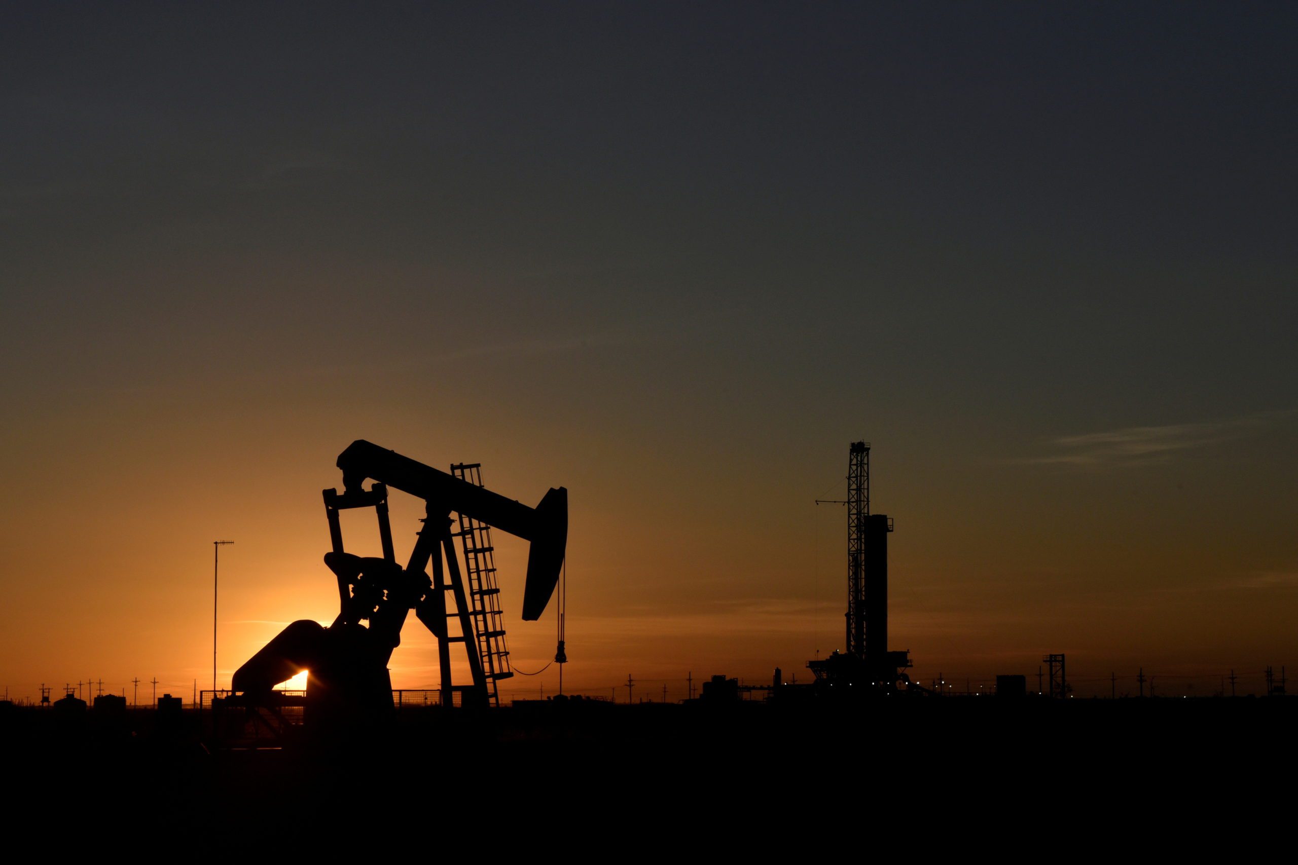 FILE PHOTO: A pump jack operates in front of a drilling rig at sunset in an oil field in Midland, Texas U.S. August 22, 2018. REUTERS/Nick Oxford/File Photo