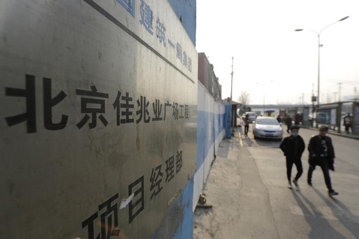 People walk past a construction site of Kaisa Plaza in Beijing, January 13, 2015. Bonds issued by Kaisa Group rose sharply on Tuesday after the embattled Chinese property developer said it had received a waiver from HSBC Holdings on a loan it failed to repay late last month. The Chinese characters in the middle of the plate reads 