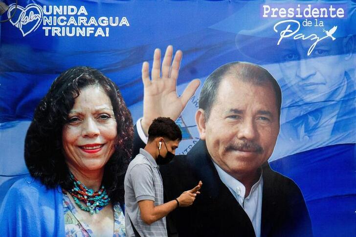 FILE PHOTO: A man checks his phone while walking by a banner promoting Nicaraguan President Daniel Ortega and Vice President Rosario Murillo as presidential election campaigning begins, in Managua, Nicaragua, September 25, 2021. REUTERS/Maynor Valenzuela NO RESALES. NO ARCHIVES/File Photo