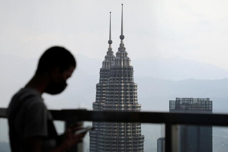 FILE PHOTO: A man wearing a protective mask uses his phone as the Petronas Twin Towers are seen in the background in Kuala Lumpur, Malaysia April 12, 2021. REUTERS/Lim Huey Teng/File Photo