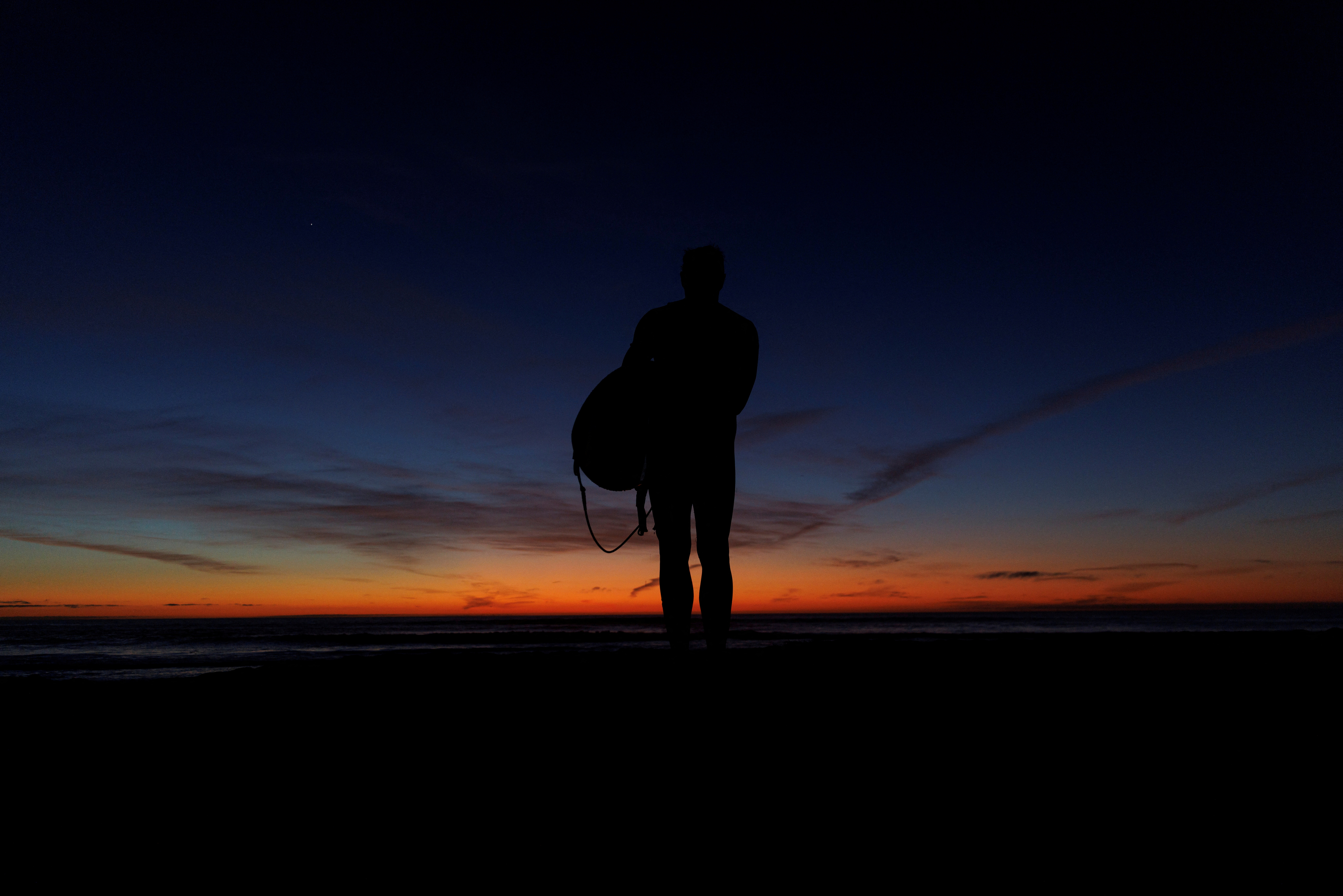 A surfer looks out at the ocean and evening sky after surfing in Encinitas, California