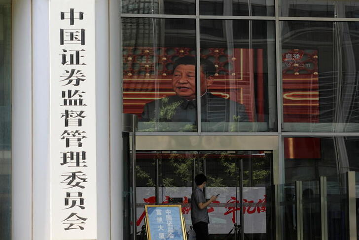 A man stands near a screen showing news footage of Chinese President Xi Jinping at the China Securities Regulatory Commission (CSRC) building on the Financial Street in Beijing, China July 9, 2021. REUTERS/Tingshu Wang