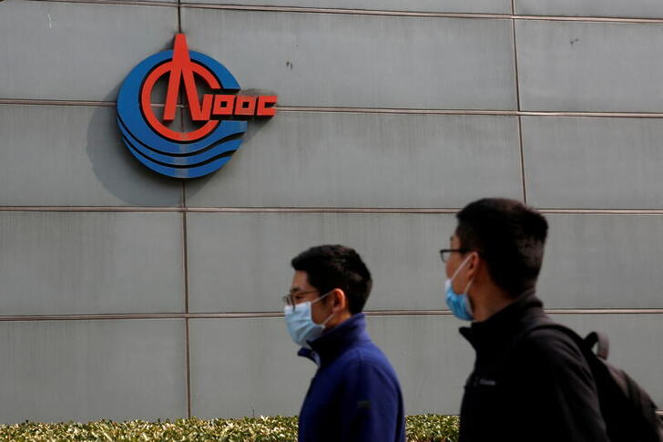 FILE PHOTO: Men wearing face masks walk past a sign of China National Offshore Oil Corp (CNOOC) outside its headquarters in Beijing, China March 8, 2021. REUTERS/Tingshu Wang/File Photo