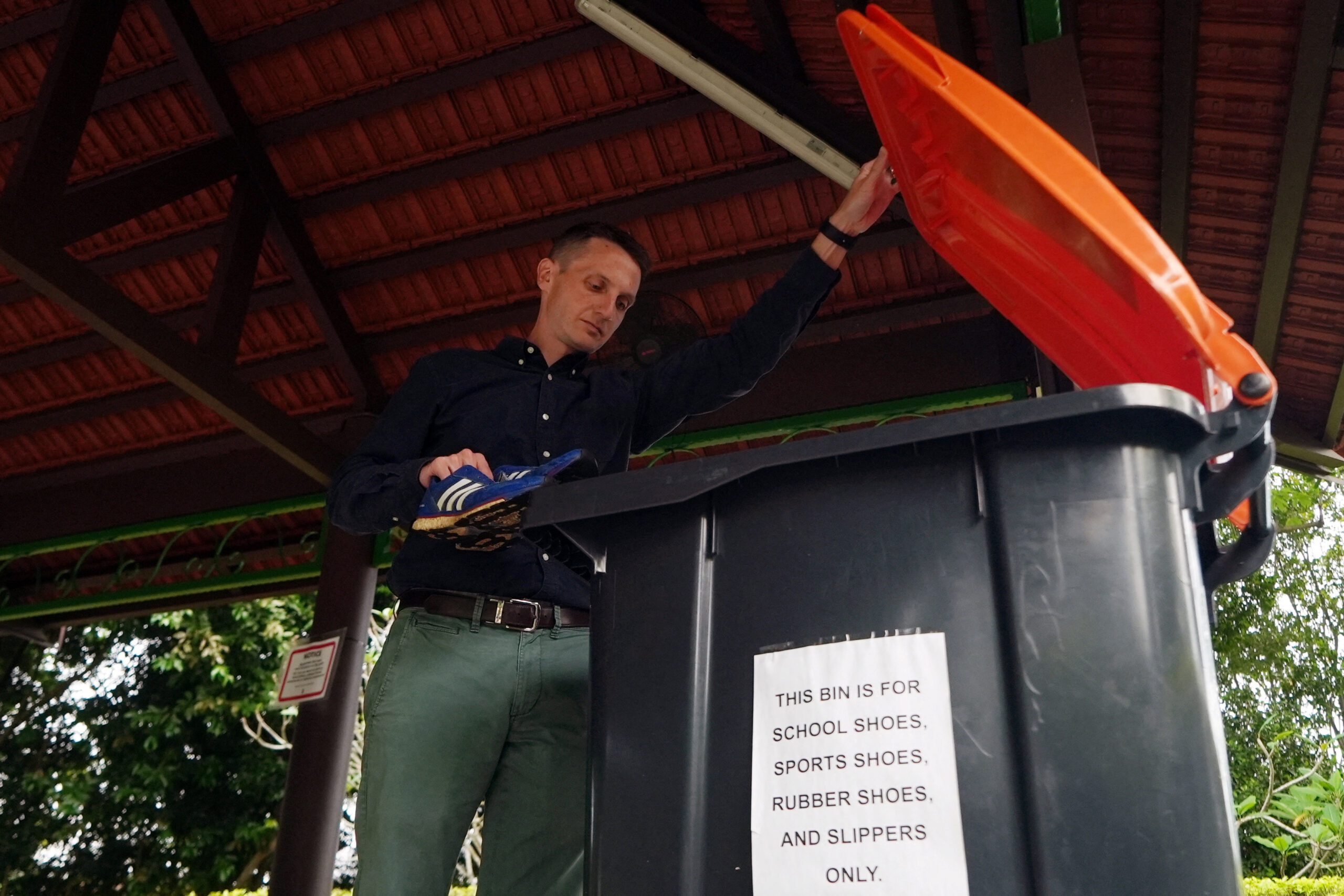 Reuters reporter Joe Brock drops off a pair of shoes containing a tracking device, at a shoe recycling bin, in a public park in Singapore, September 7, 2022. REUTERS/Joseph Campbell