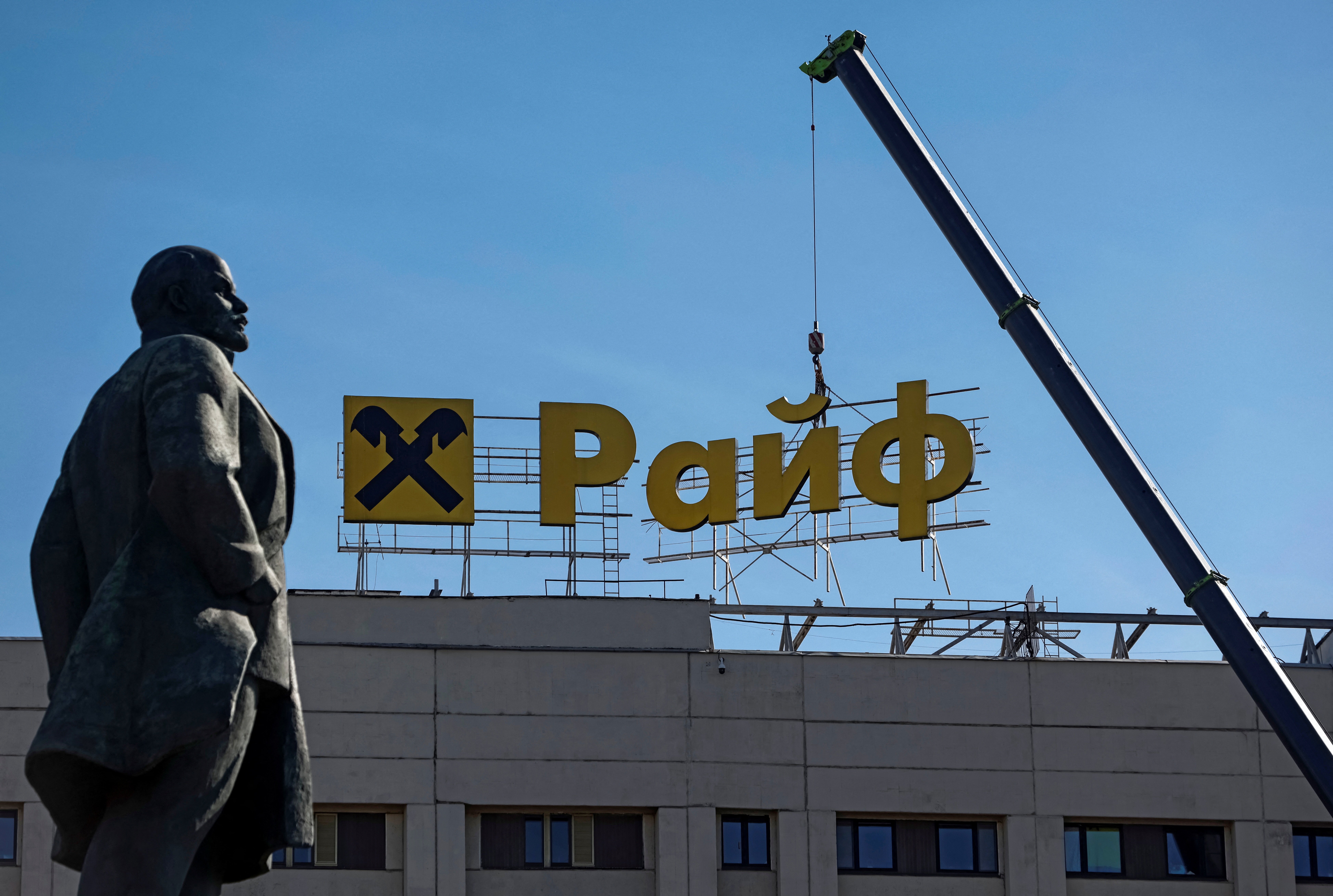 Workers use a crane to dismantle a signboard advertising Raiffeisen Bank from a building, as a monument to Soviet state founder Vladimir Lenin is seen in the foreground, in Moscow, Russia April 14, 2023. REUTERS/Maxim Shemetov